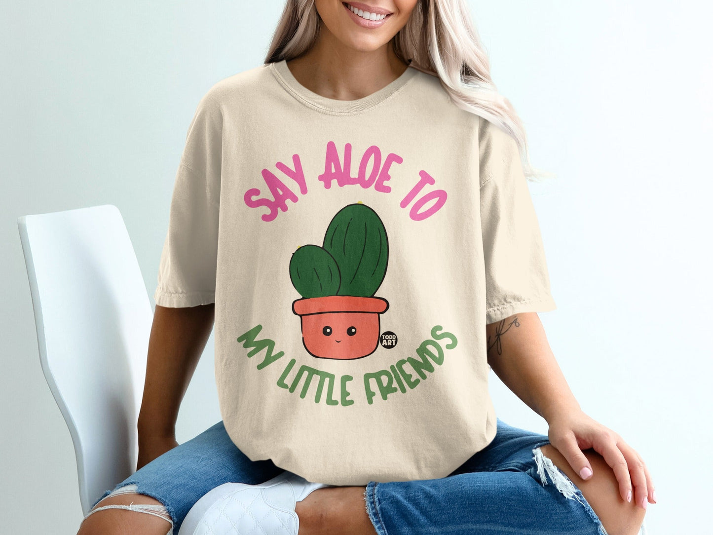 "Say Aloe to My Little Friends" text on a t-shirt with a smiling cartoon cactus in a pot.