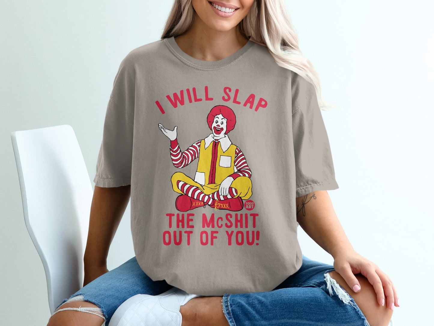 Ronald McDonald seated, wearing a shirt that reads "I WILL SLAP THE MCSHIT OUT OF YOU!".