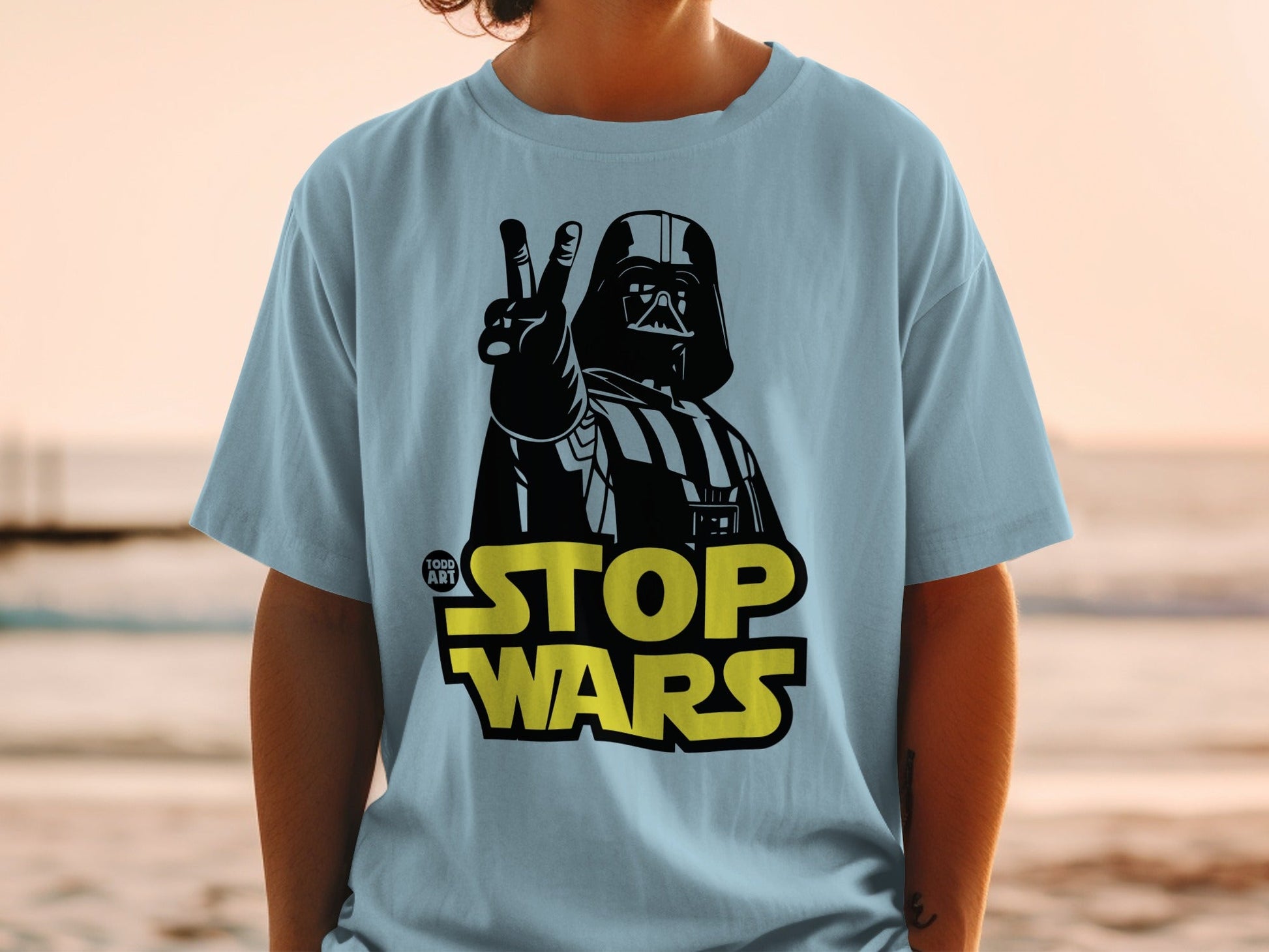 Light blue t-shirt with Darth Vader giving peace sign and "STOP WARS" text.