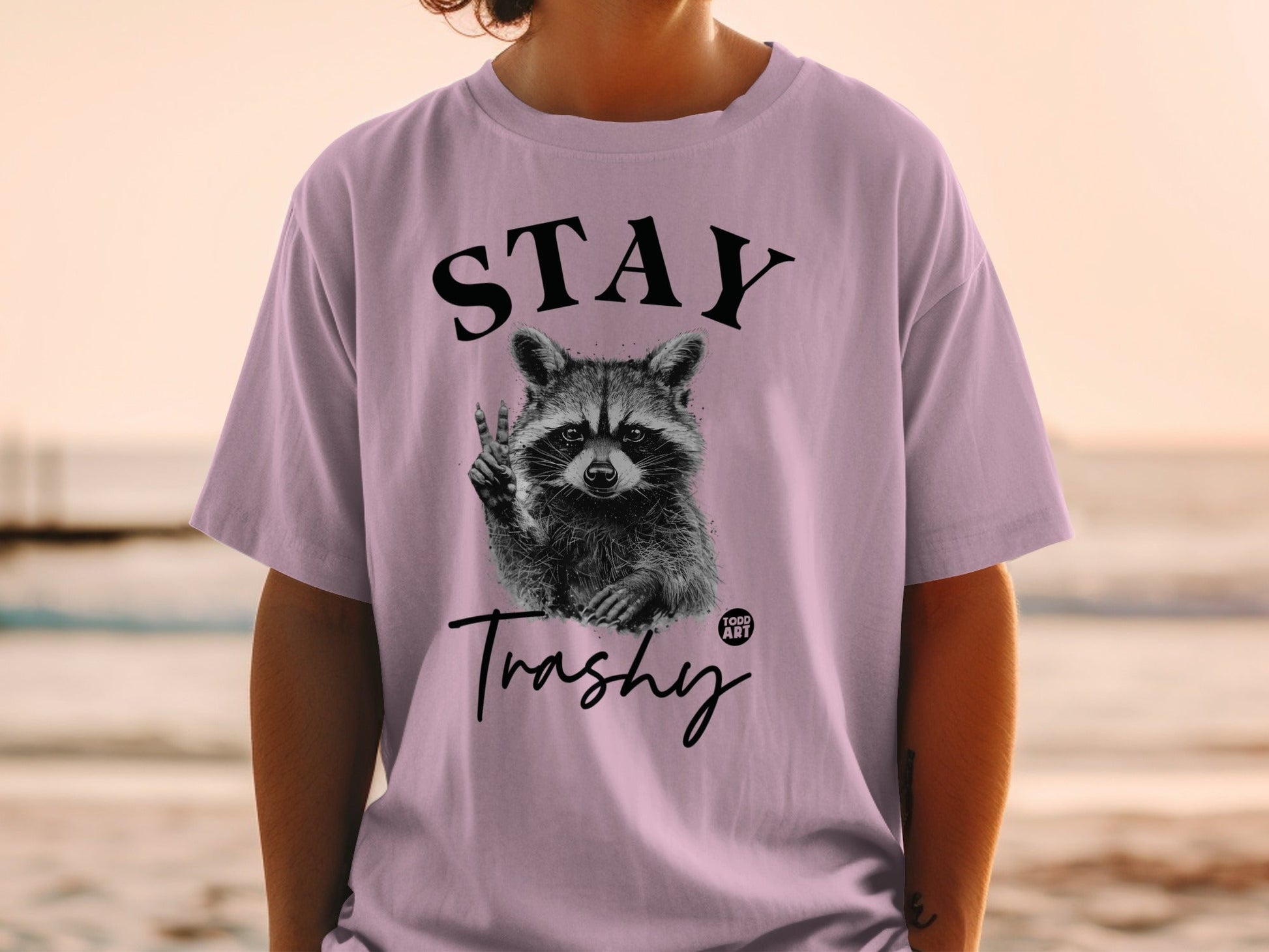 Purple t-shirt with raccoon giving peace sign and "STAY Trashy" text.