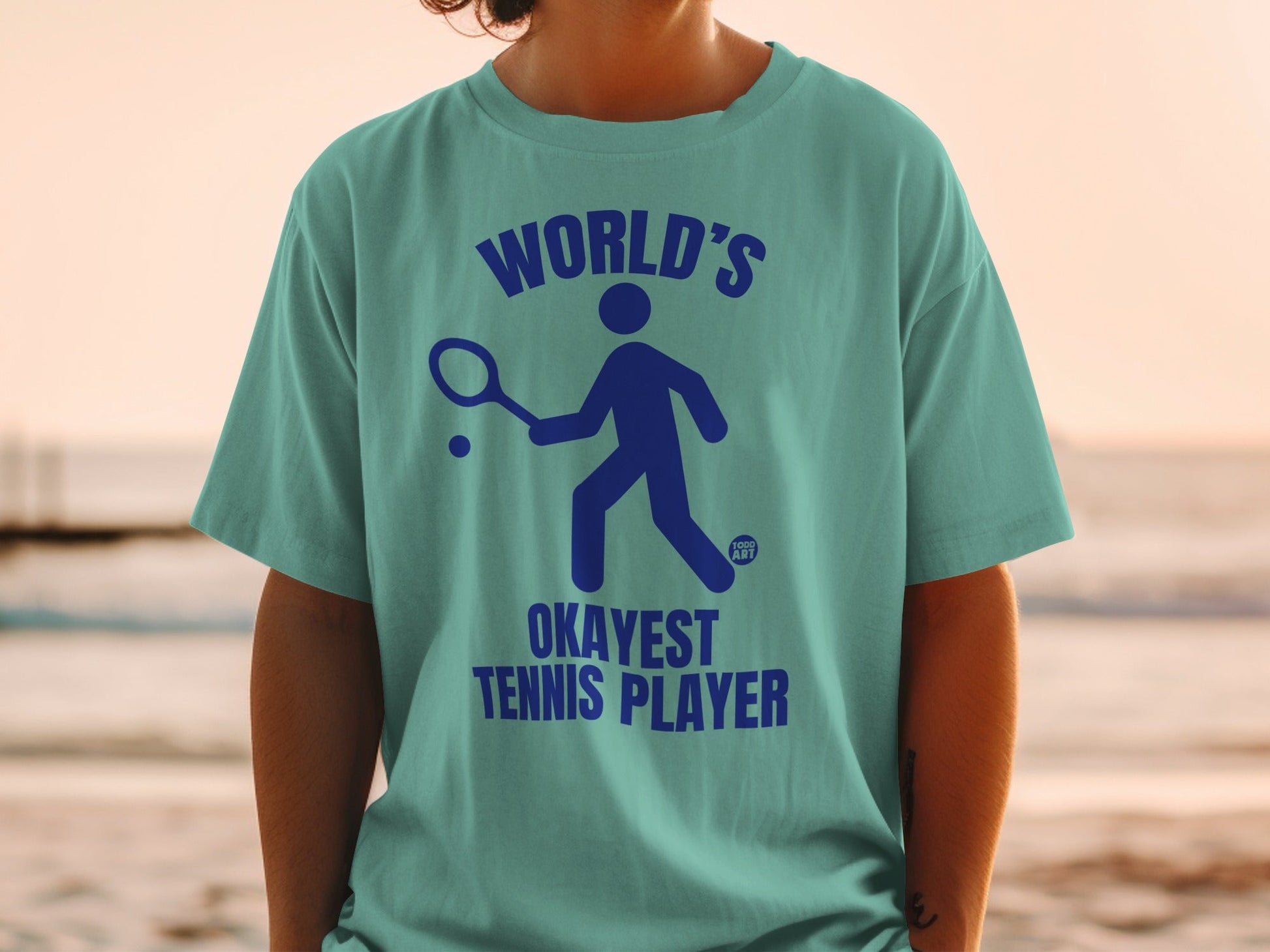 Teal t-shirt with "WORLD'S OKAYEST TENNIS PLAYER" text and a stick figure playing tennis.