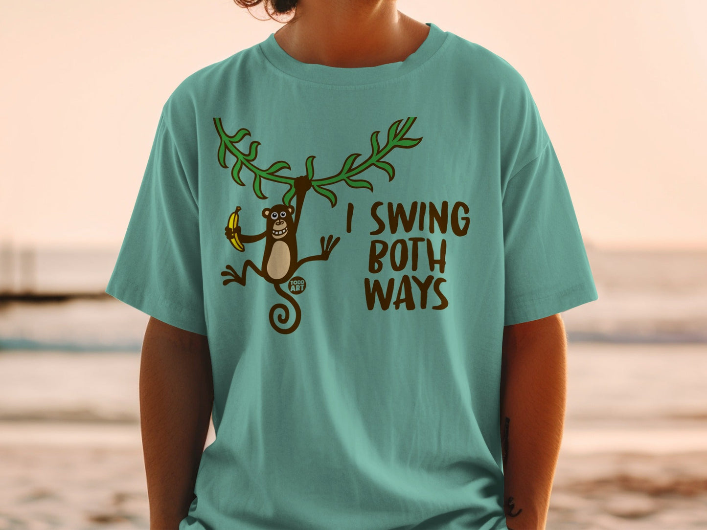 Teal t-shirt with a monkey swinging from vines holding a banana and the text "I SWING BOTH WAYS".