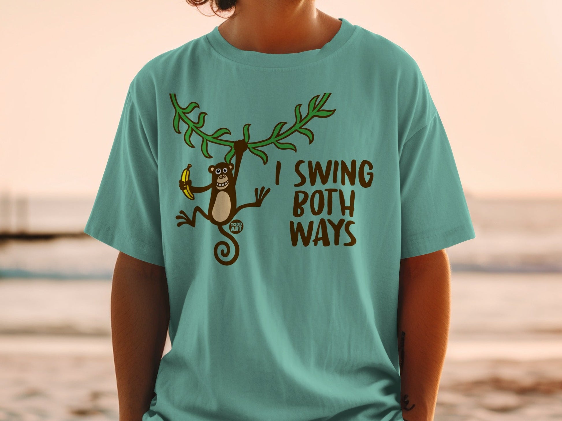 Teal t-shirt with a monkey swinging from vines holding a banana and the text "I SWING BOTH WAYS".