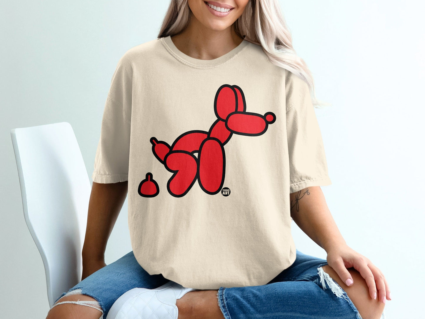 Cream t-shirt with a red balloon dog and a small brown shape next to it.