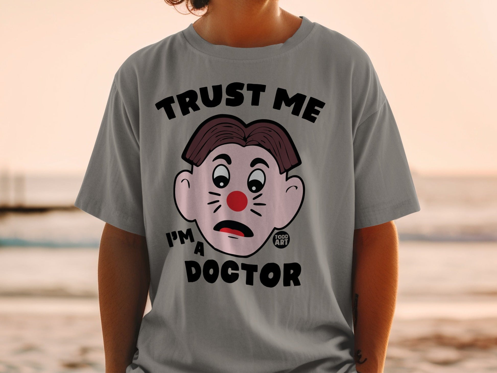 Grey t-shirt with cartoon face and "TRUST ME I'M A DOCTOR" text.