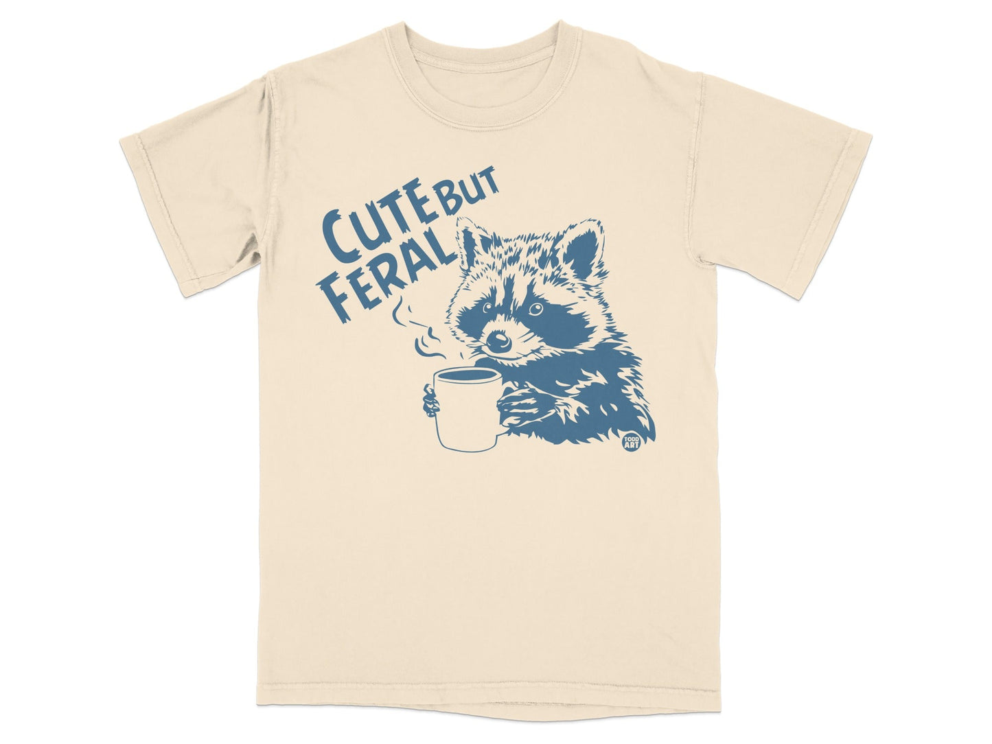 Cream t-shirt with blue raccoon drinking coffee, "Cute But Feral" text.