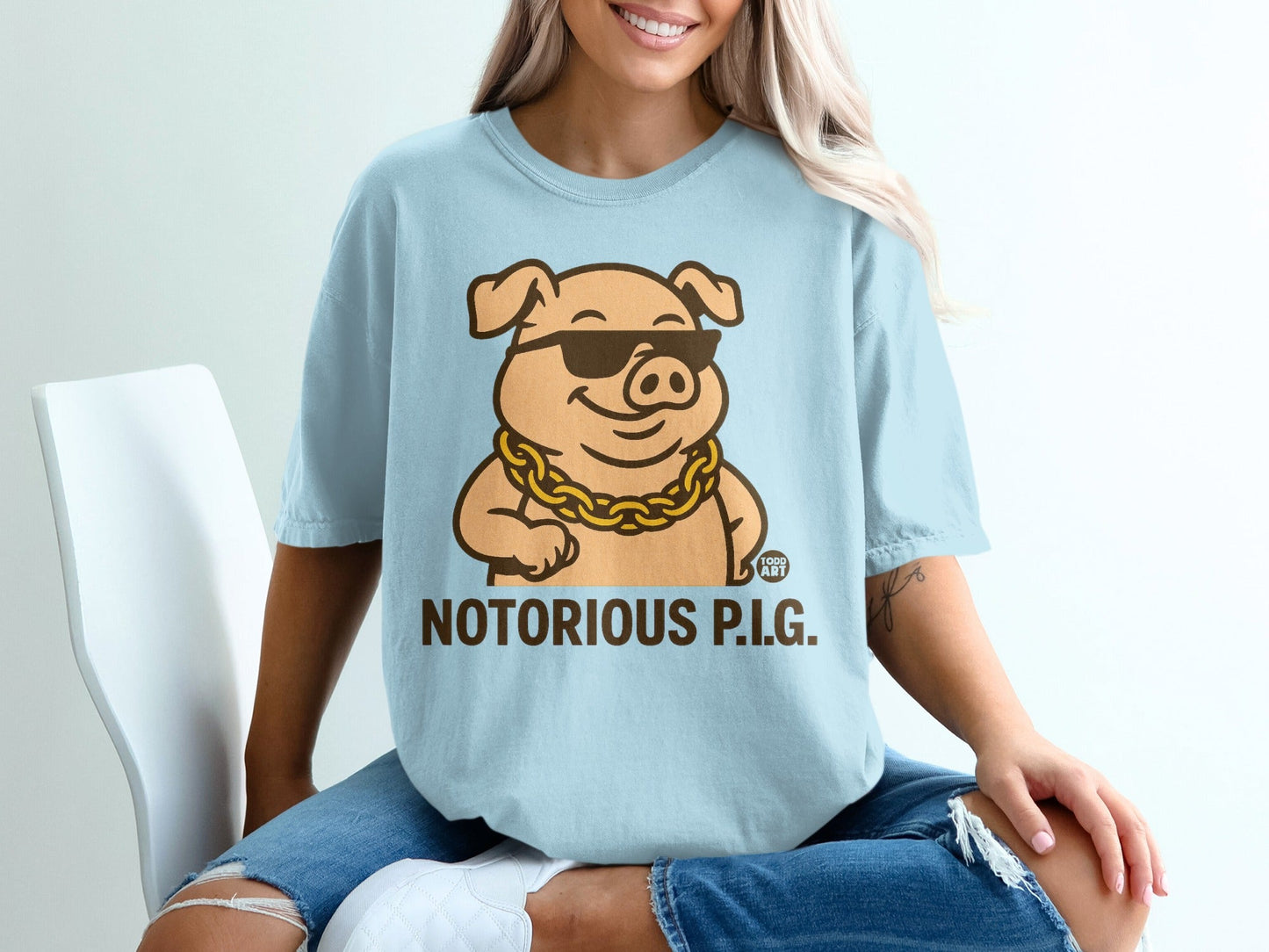Light blue t-shirt with cartoon pig wearing sunglasses and gold chain, text "NOTORIOUS P.I.G."
