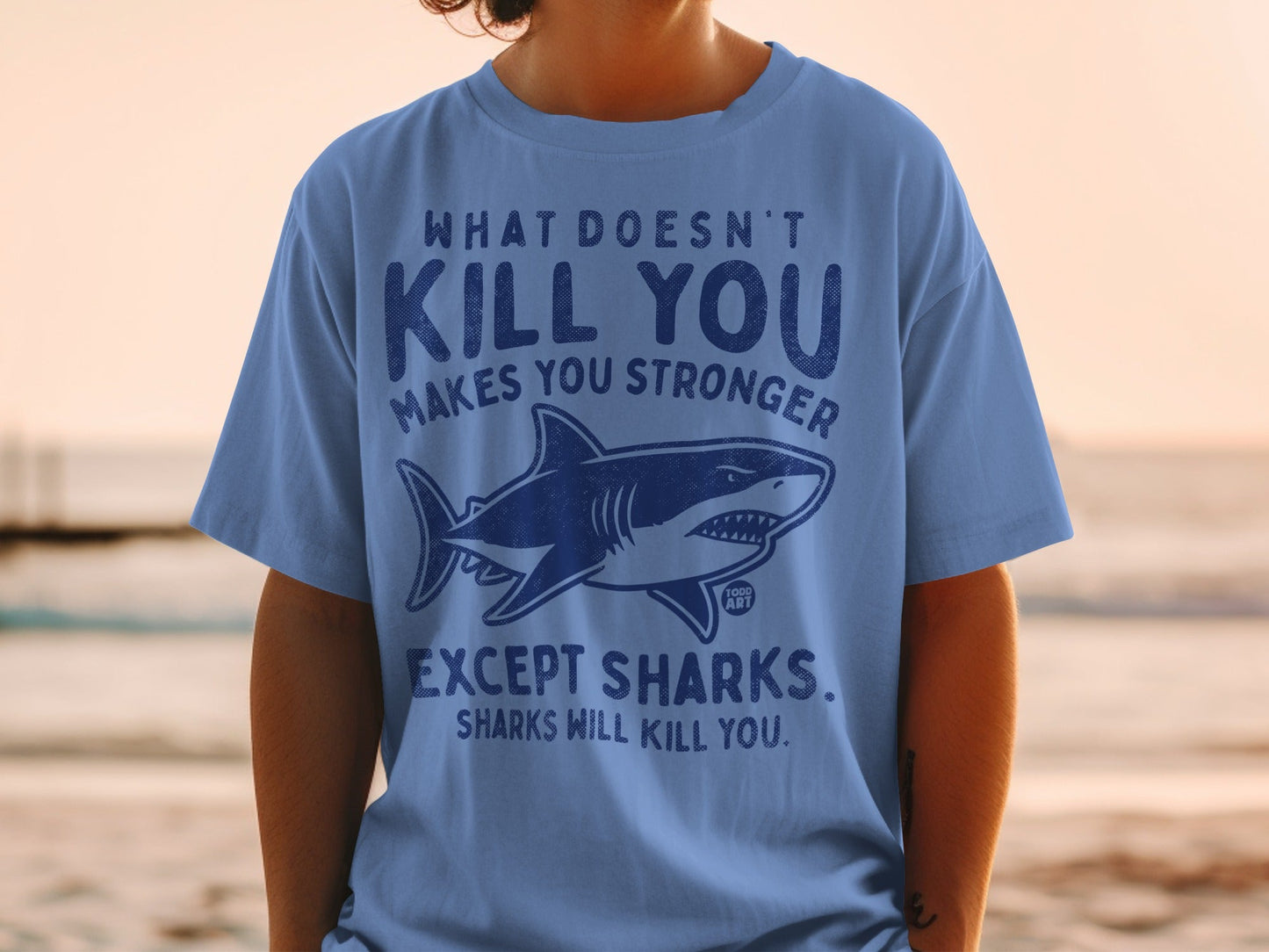 Blue t-shirt with shark graphic and text "What doesn't kill you makes you stronger except sharks."