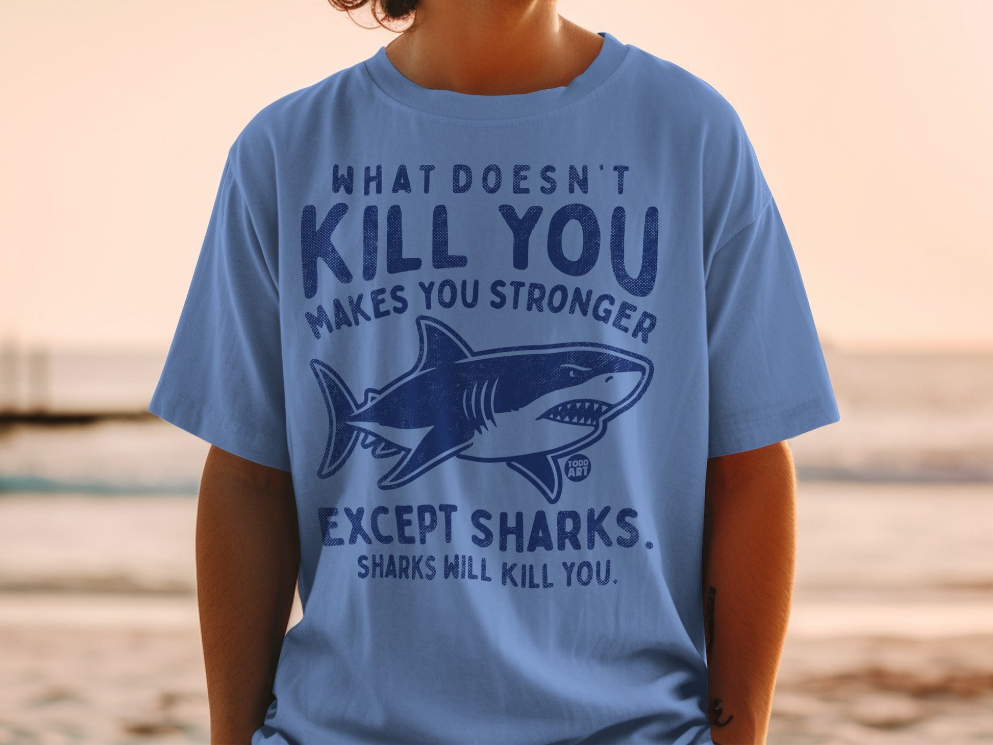 Blue t-shirt with shark graphic and text "What doesn't kill you makes you stronger except sharks."