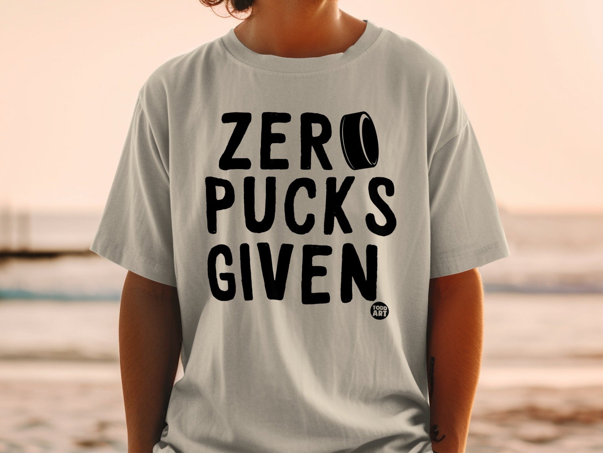 Gray t-shirt with "ZERO PUCKS GIVEN" text and hockey puck graphic.
