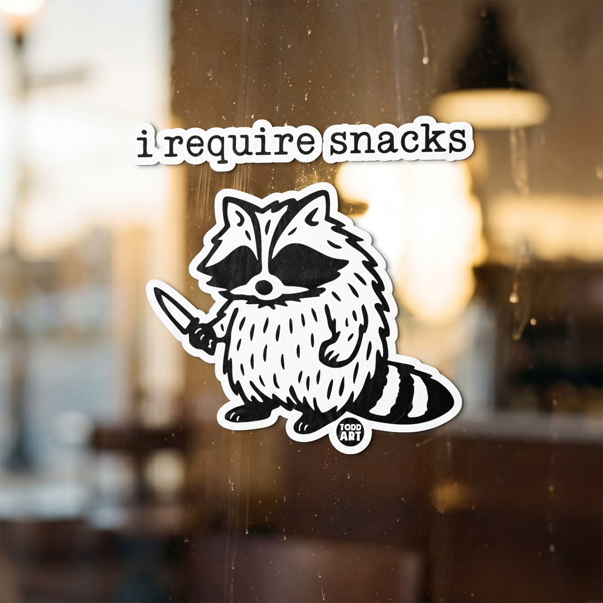 Sticker of a raccoon holding a knife with "i require snacks" text above.