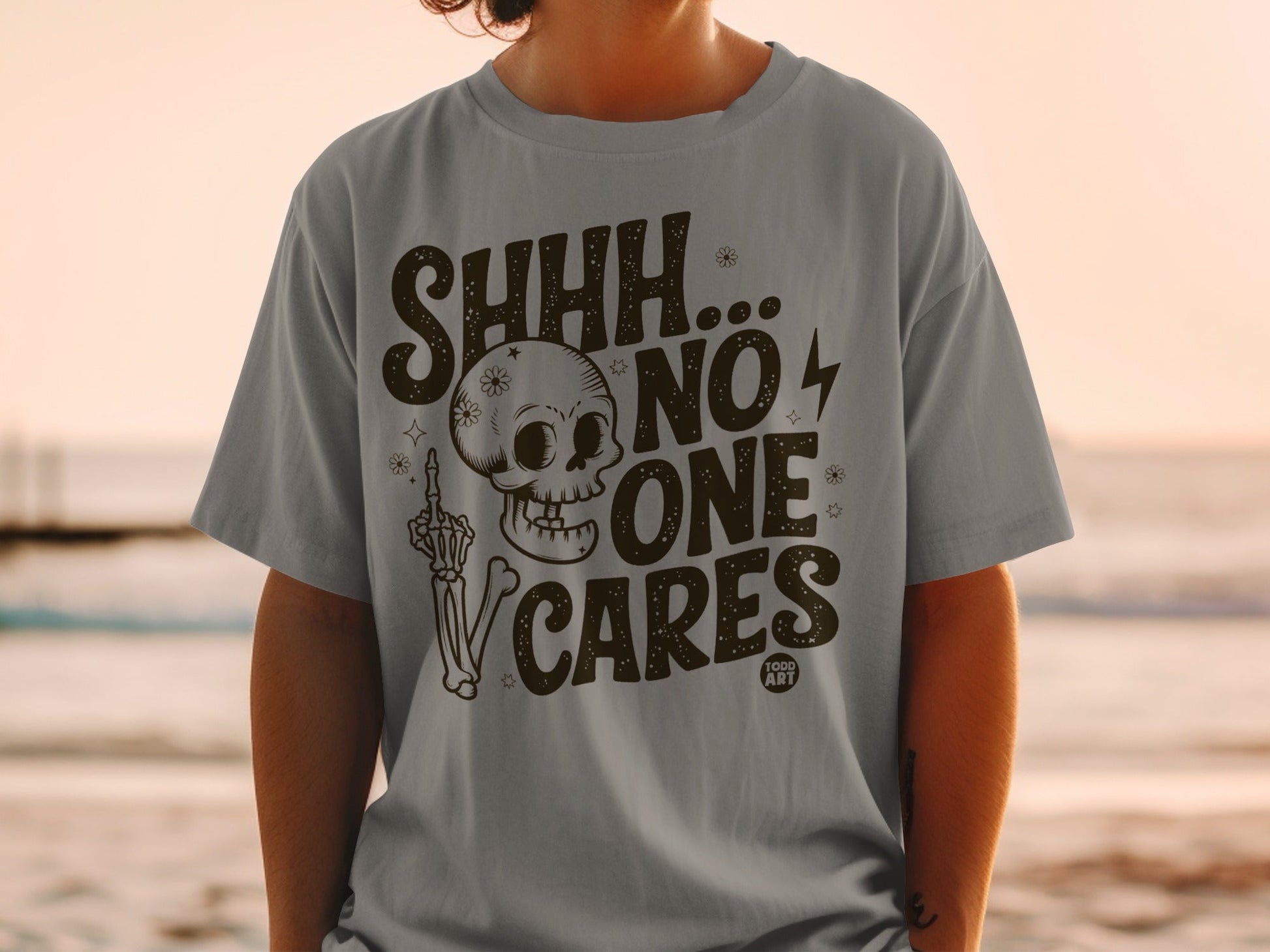 Gray t-shirt with skull, skeleton hand, and "SHHH... NO ONE CARES" text.