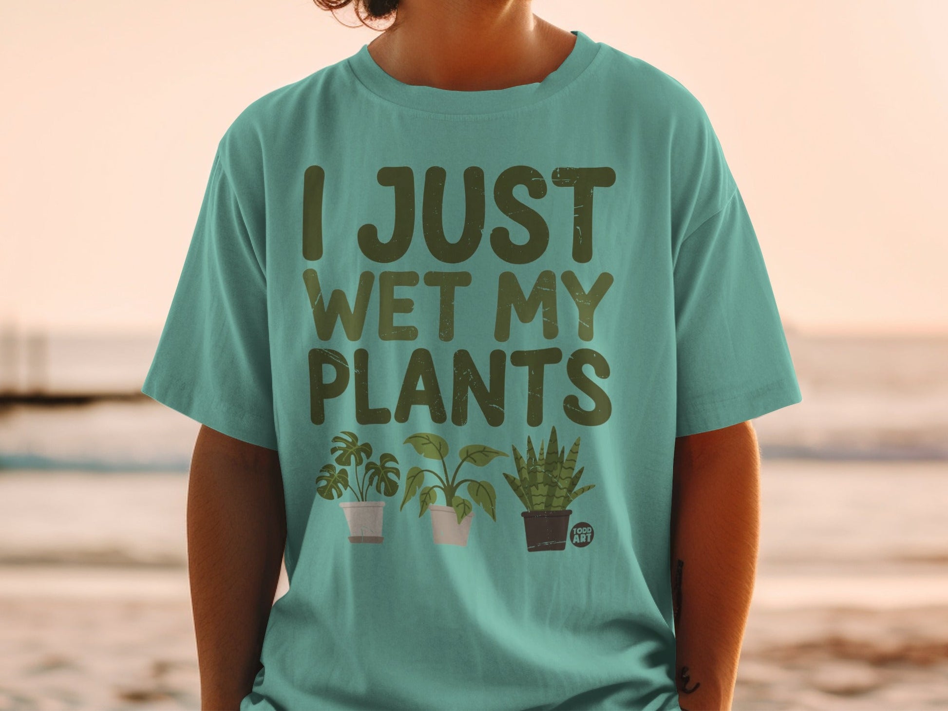 Teal t-shirt with "I JUST WET MY PLANTS" and three illustrated potted plants.