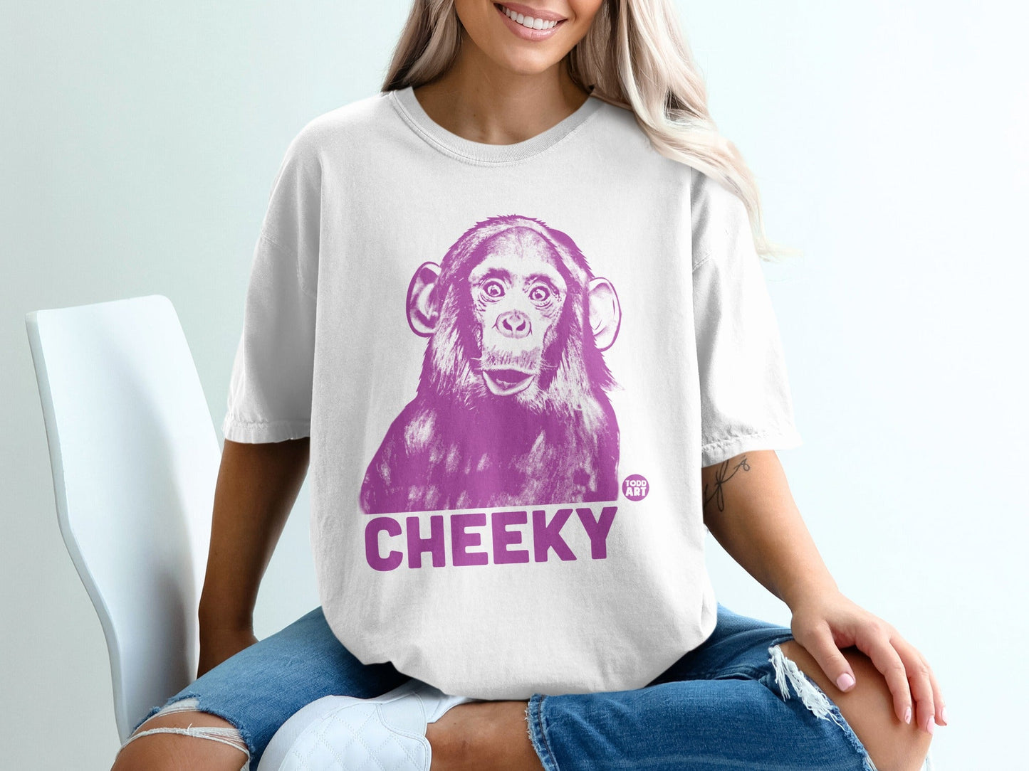 White t-shirt with a purple graphic of a chimpanzee face and the word "CHEEKY".