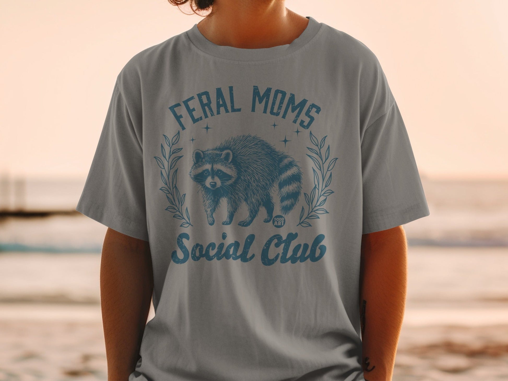 Grey t-shirt with "FERAL MOMS Social Club" and raccoon graphic.