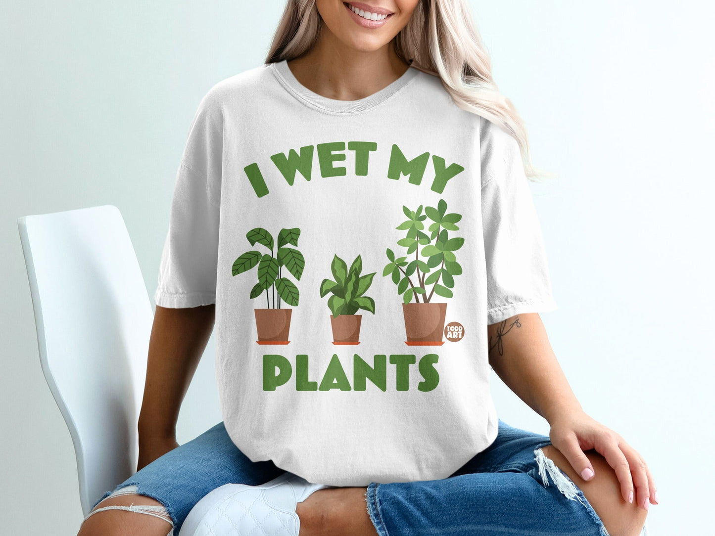 White t-shirt with green text "I WET MY PLANTS" and three potted plants.