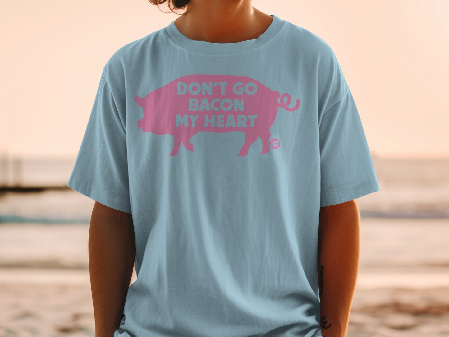 Light blue t-shirt with a pink pig silhouette and "Don't Go Bacon My Heart" text.