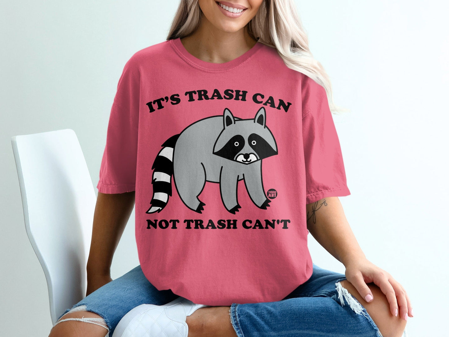 Pink t-shirt with a raccoon graphic and text "It's trash can not trash can't".