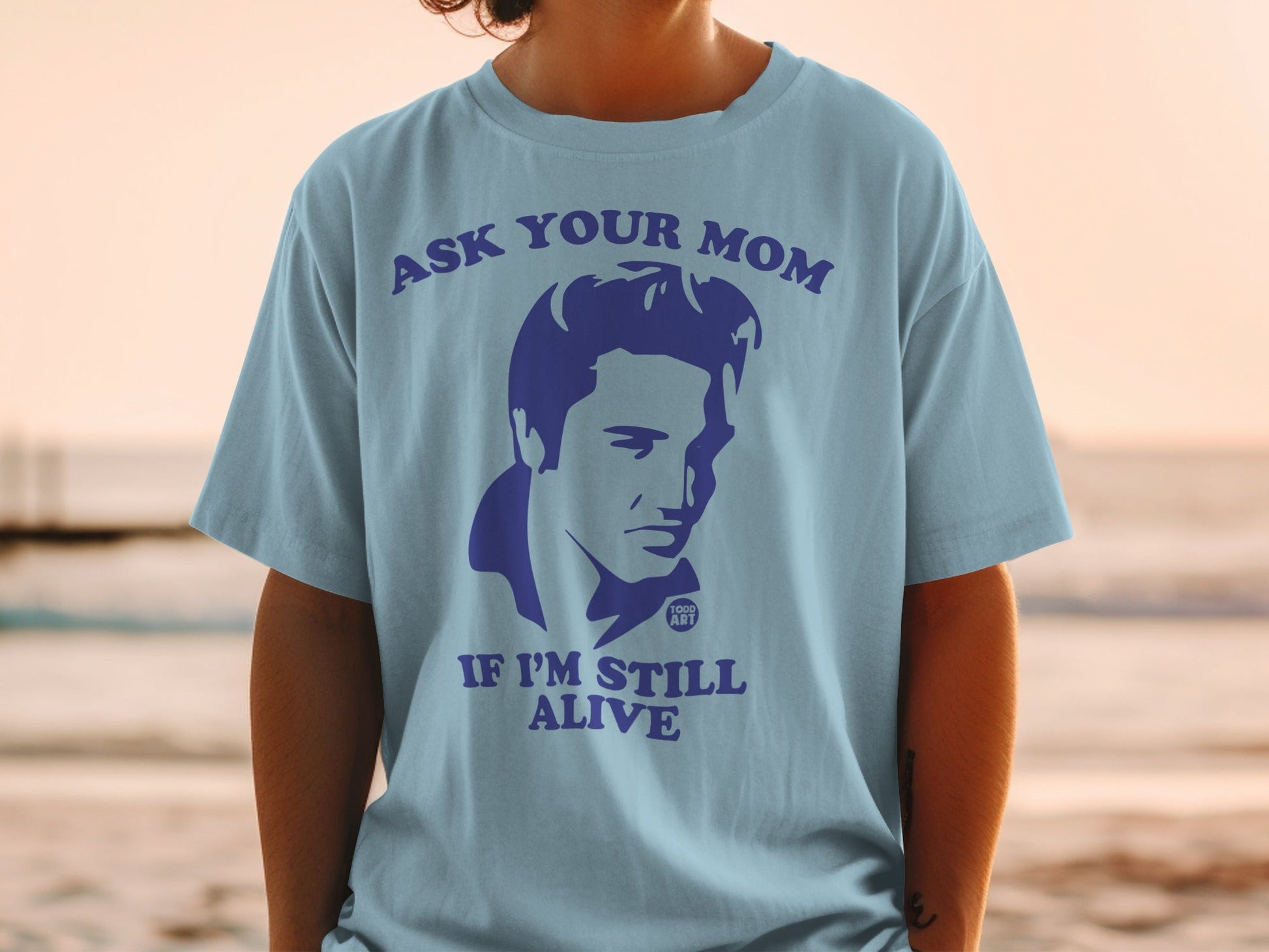 Light blue t-shirt with an Elvis graphic and "Ask Your Mom If I'm Still Alive" text.