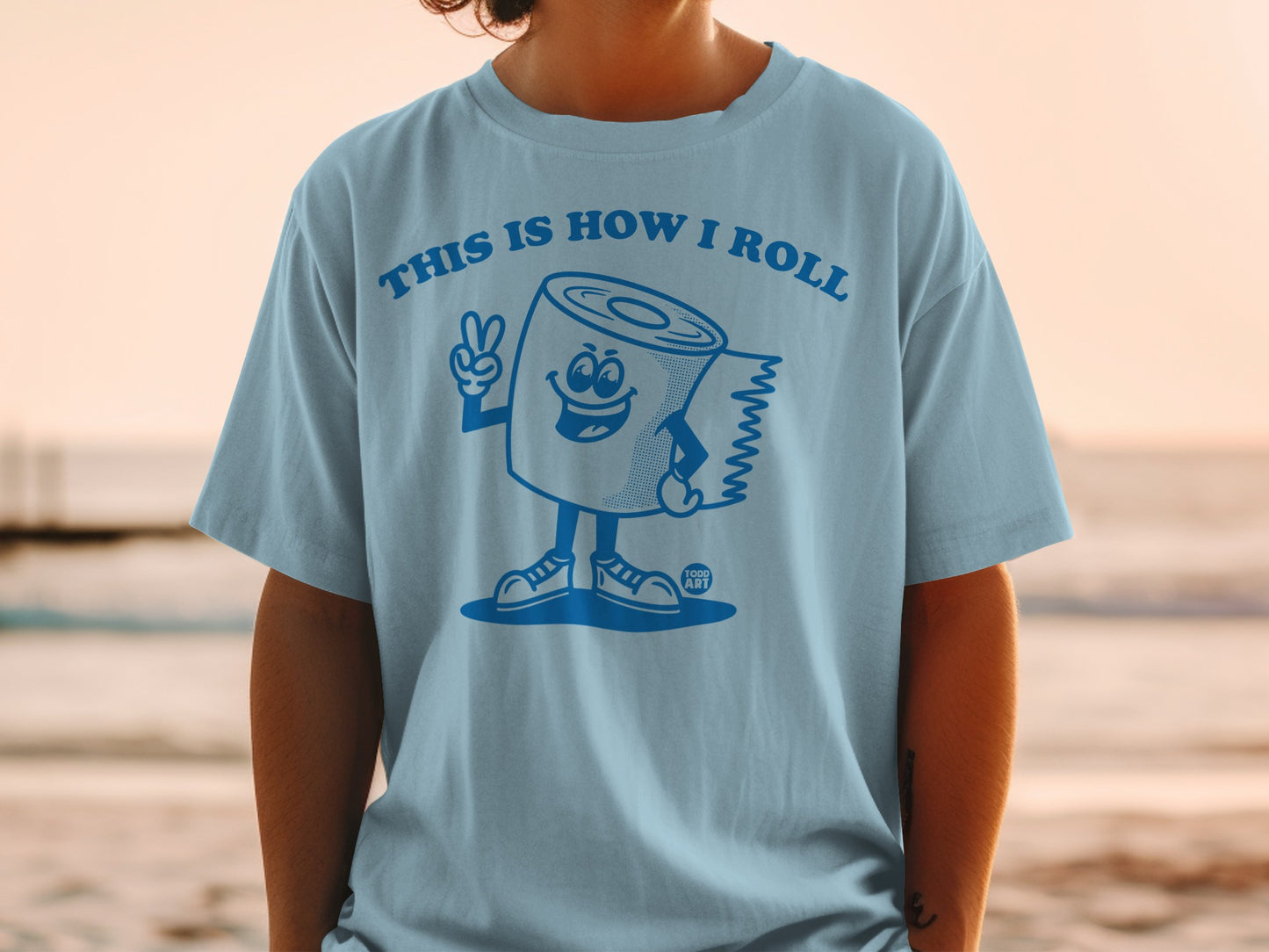 Light blue t-shirt with a cartoon toilet paper roll character giving a peace sign.