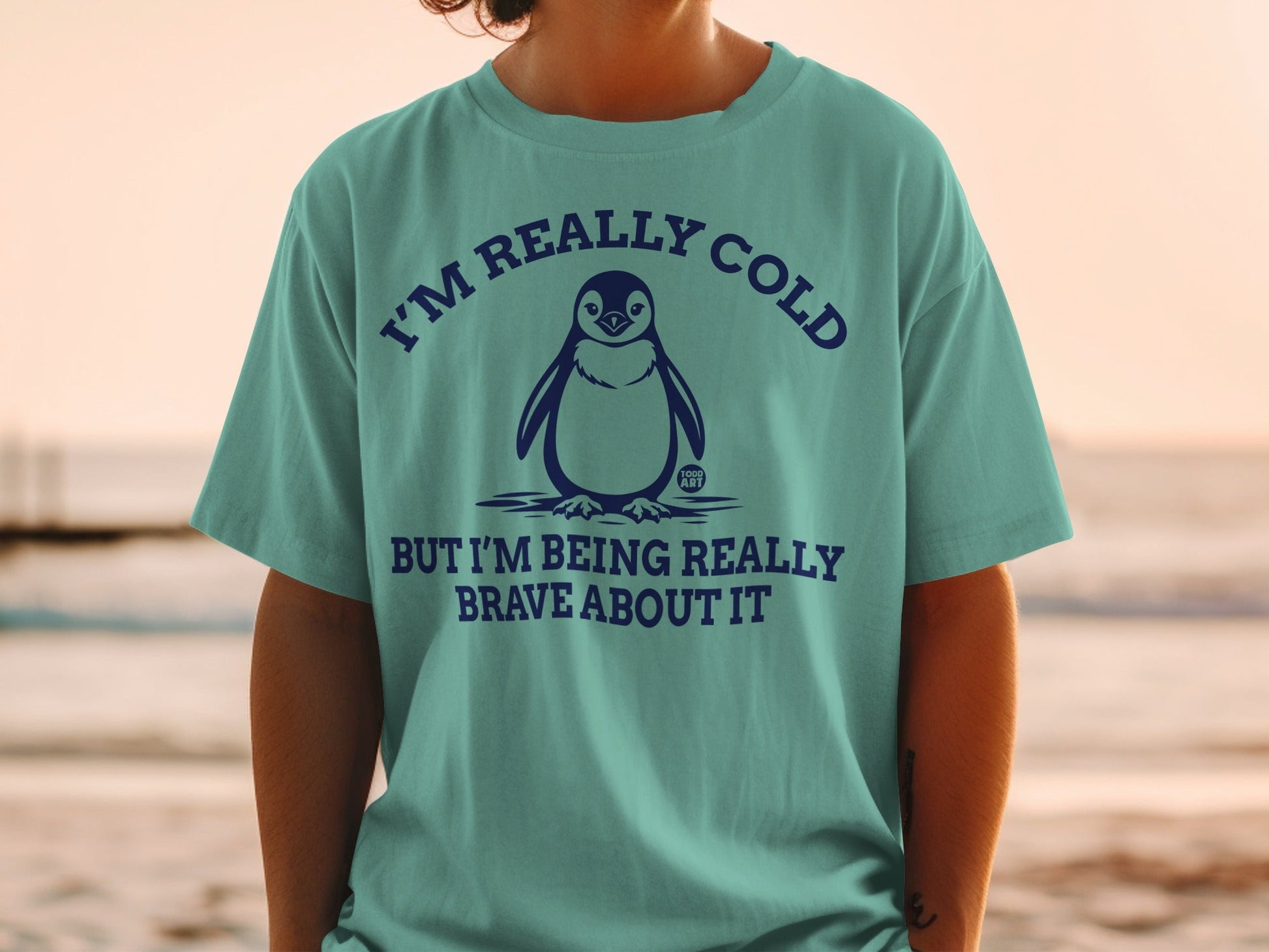 Teal t-shirt with penguin graphic and text "I'm really cold but I'm being really brave about it."