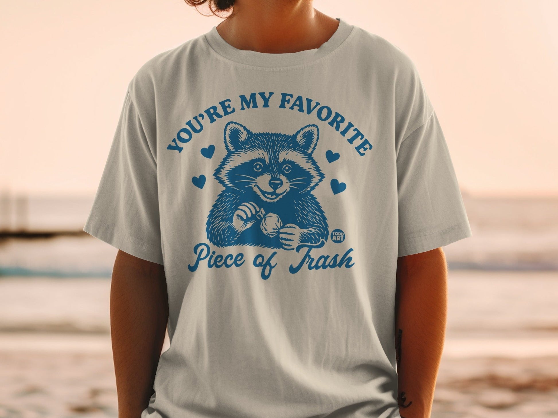 T-shirt with raccoon graphic and text "YOU'RE MY FAVORITE Piece of Trash".