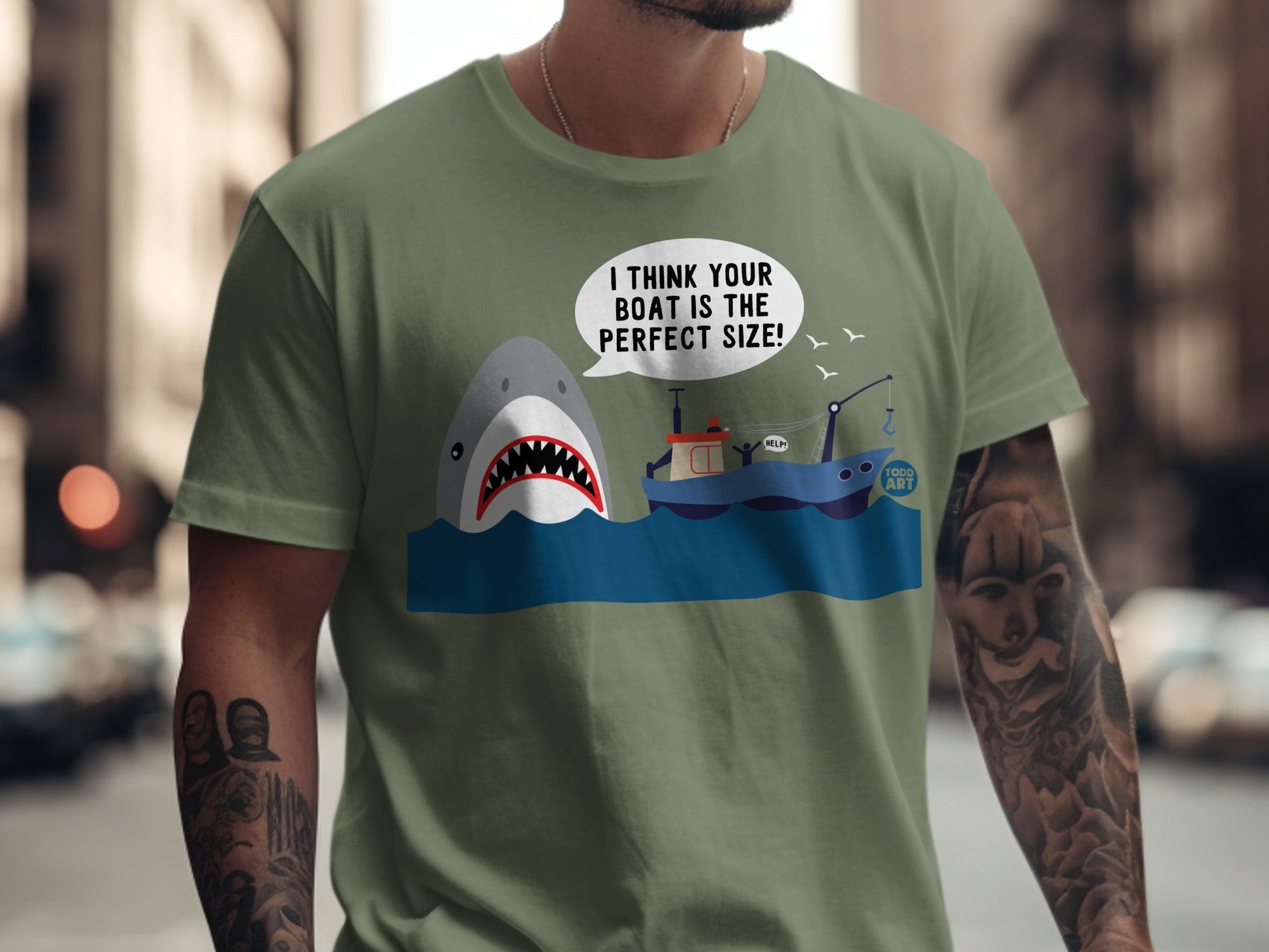 Green t-shirt with cartoon shark near a fishing boat, speech bubble says "I THINK YOUR BOAT IS THE PERFECT SIZE!".