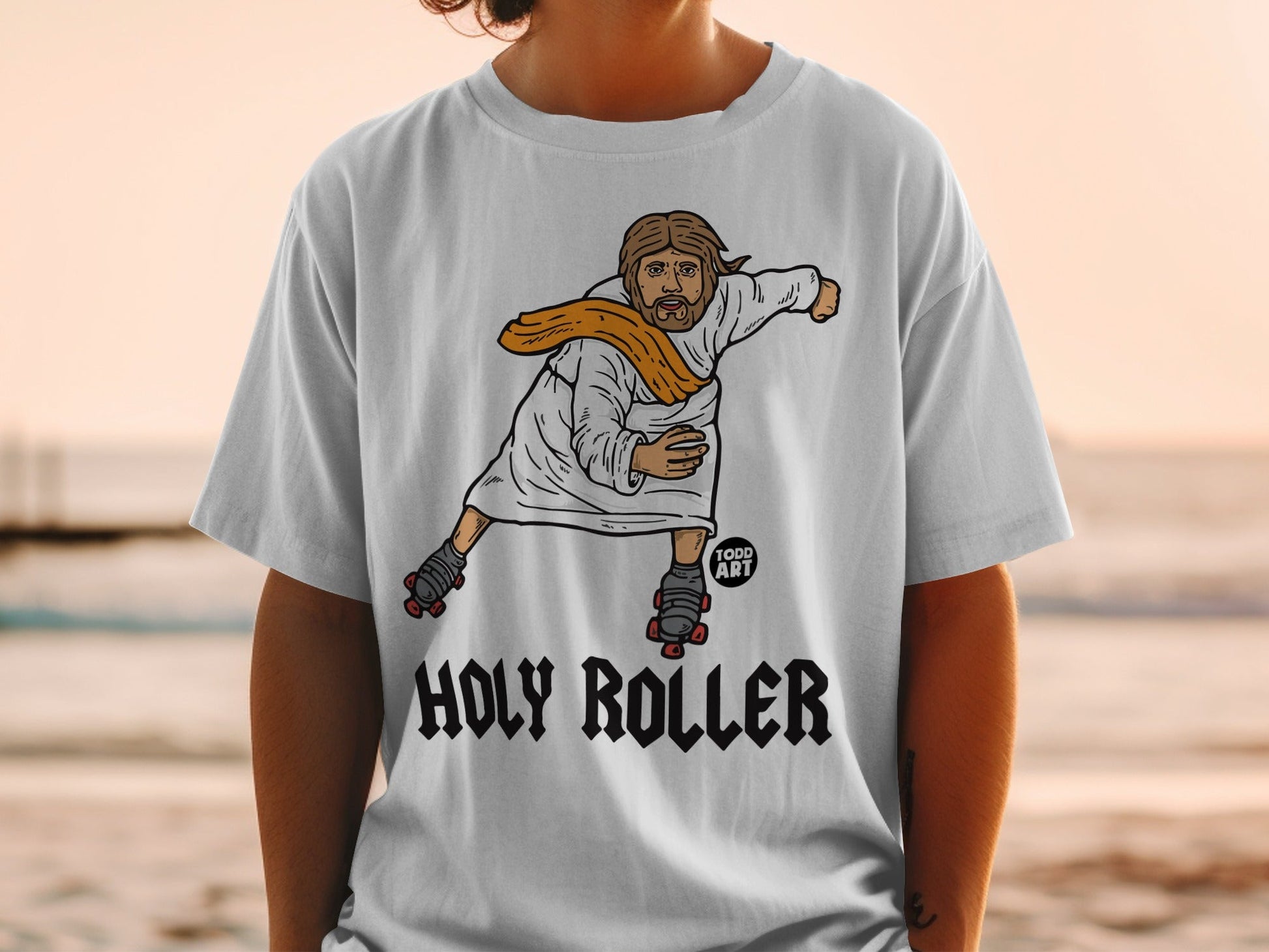 T-shirt with cartoon Jesus on roller skates, text "HOLY ROLLER" and "TODD ART".