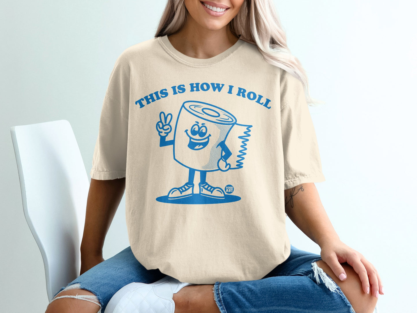 Cream t-shirt with blue text and cartoon toilet paper character.