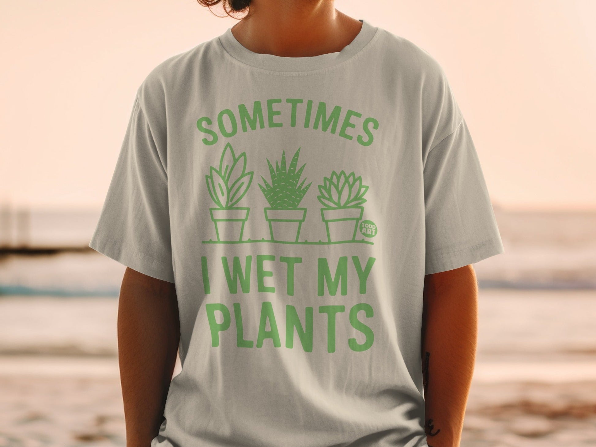Light green t-shirt with cartoon plants and text "SOMETIMES I WET MY PLANTS".