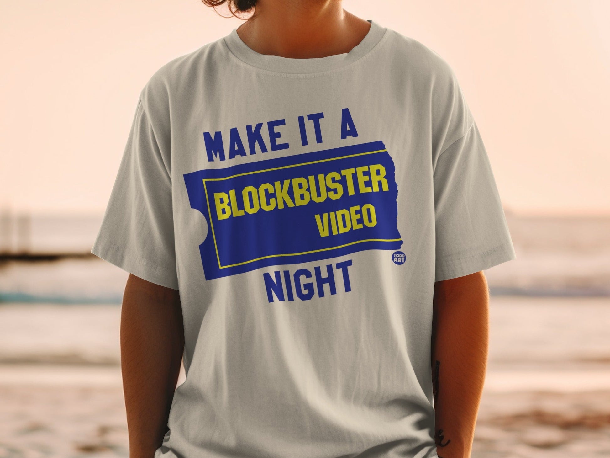 Light grey t-shirt with "MAKE IT A BLOCKBUSTER NIGHT" text on a blue ticket.