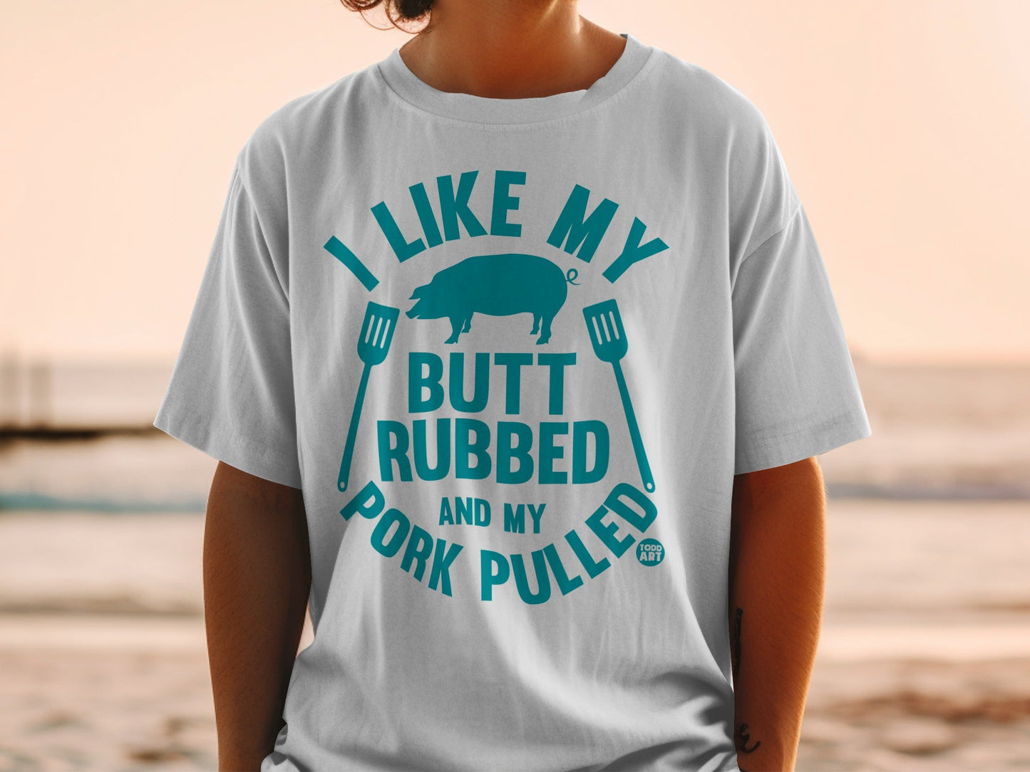 White t-shirt with teal text and pig graphic: "I like my butt rubbed and my pork pulled."