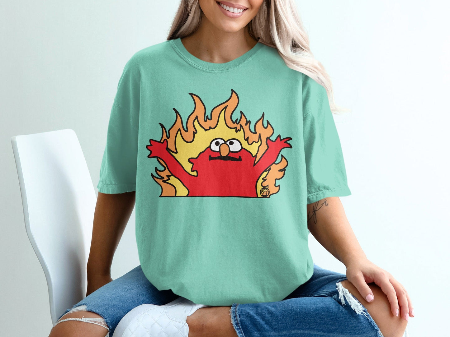Elmo on fire with flames behind him, on a teal t-shirt.