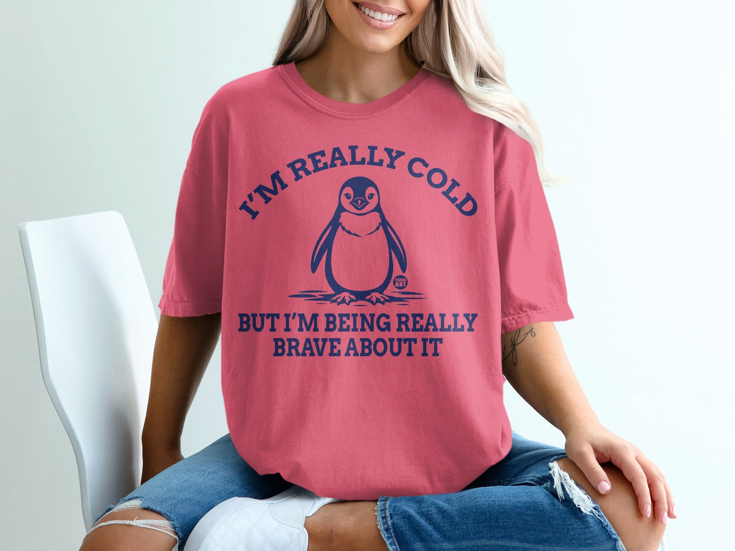Coral t-shirt with penguin graphic and text "I'm really cold but I'm being really brave about it".