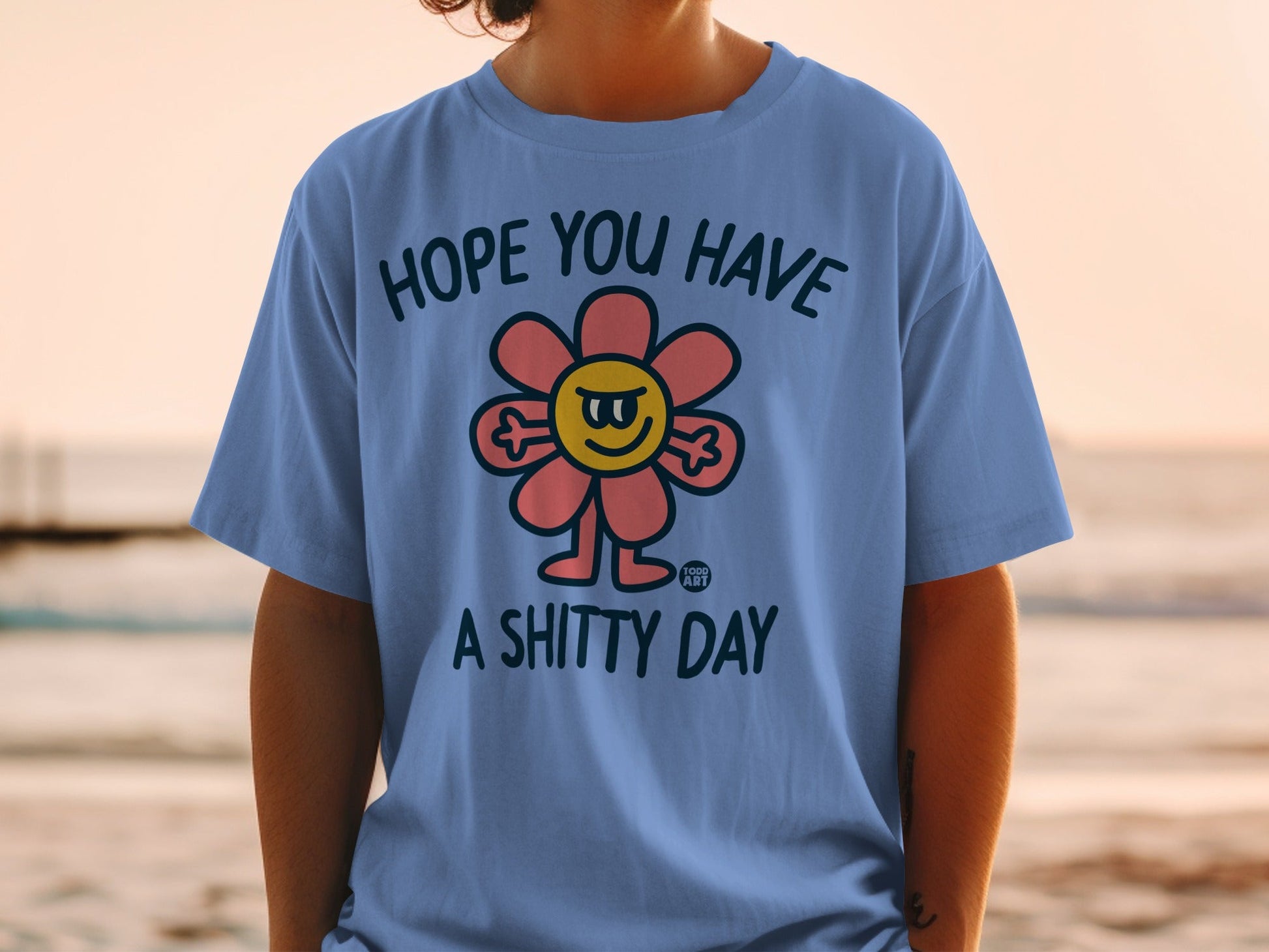 Blue t-shirt with a grumpy flower illustration and text "HOPE YOU HAVE A SHITTY DAY".