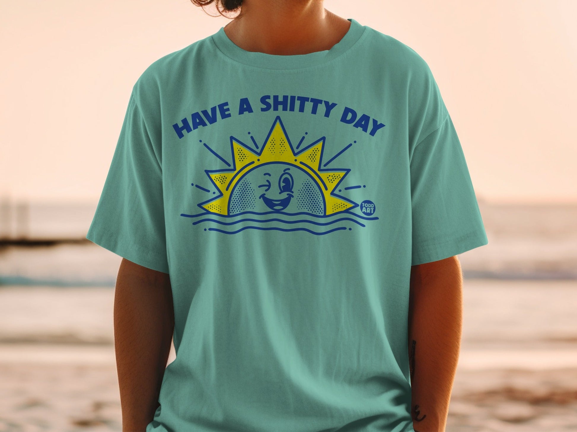 T-shirt with "HAVE A SHITTY DAY" text and a winking sun over waves.