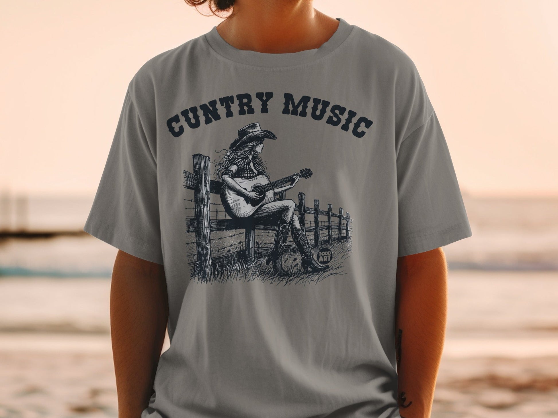 T-shirt graphic: woman in cowboy hat playing guitar by fence.