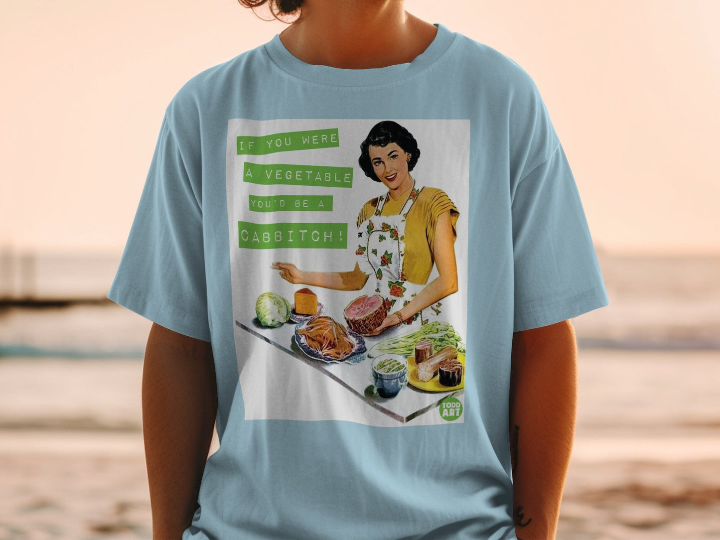 T-shirt with vintage illustration: woman, ham, cabbage, carrots, and text "If you were a vegetable you'd be a cabbitch!".