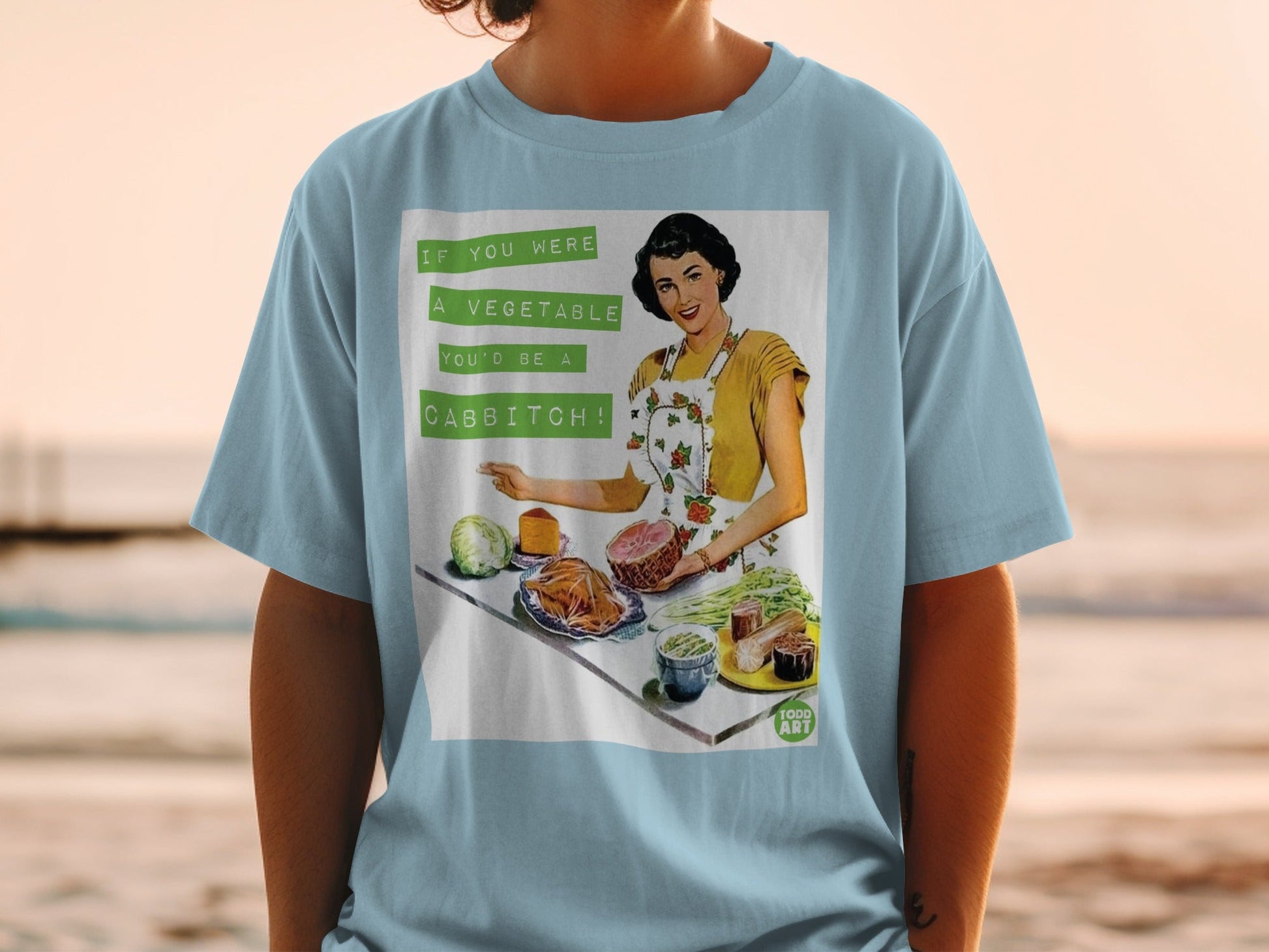 T-shirt with vintage illustration: woman, ham, cabbage, carrots, and text "If you were a vegetable you'd be a cabbitch!".
