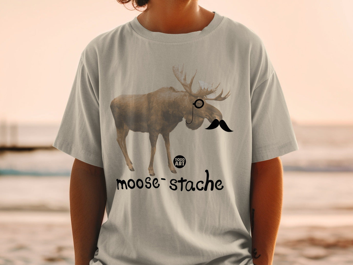 T-shirt with a moose wearing a monocle and mustache, text reads "moose-stache".