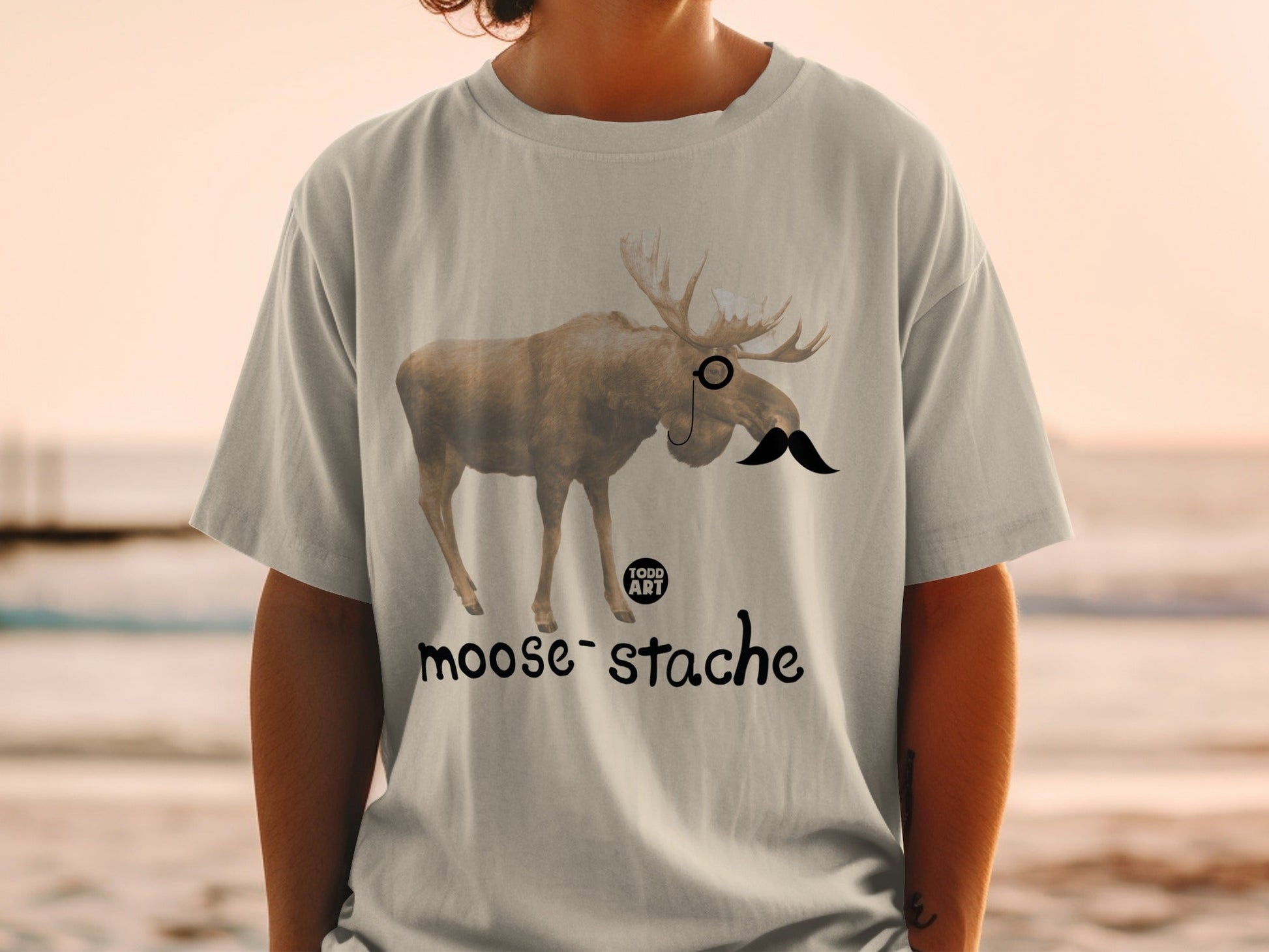 T-shirt with a moose wearing a monocle and mustache, text reads "moose-stache".