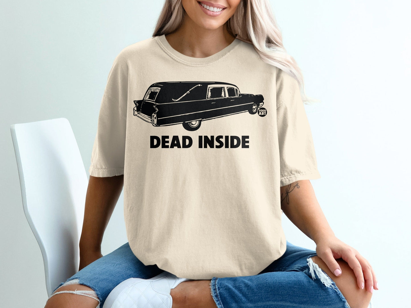 Beige t-shirt with a black hearse graphic and text "DEAD INSIDE".
