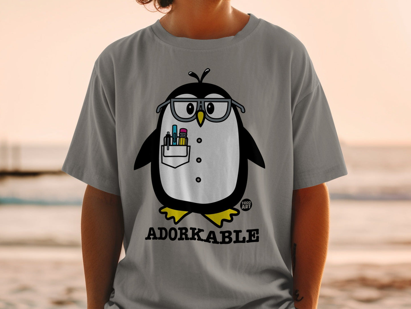 Grey t-shirt with cartoon penguin wearing glasses and holding pens.