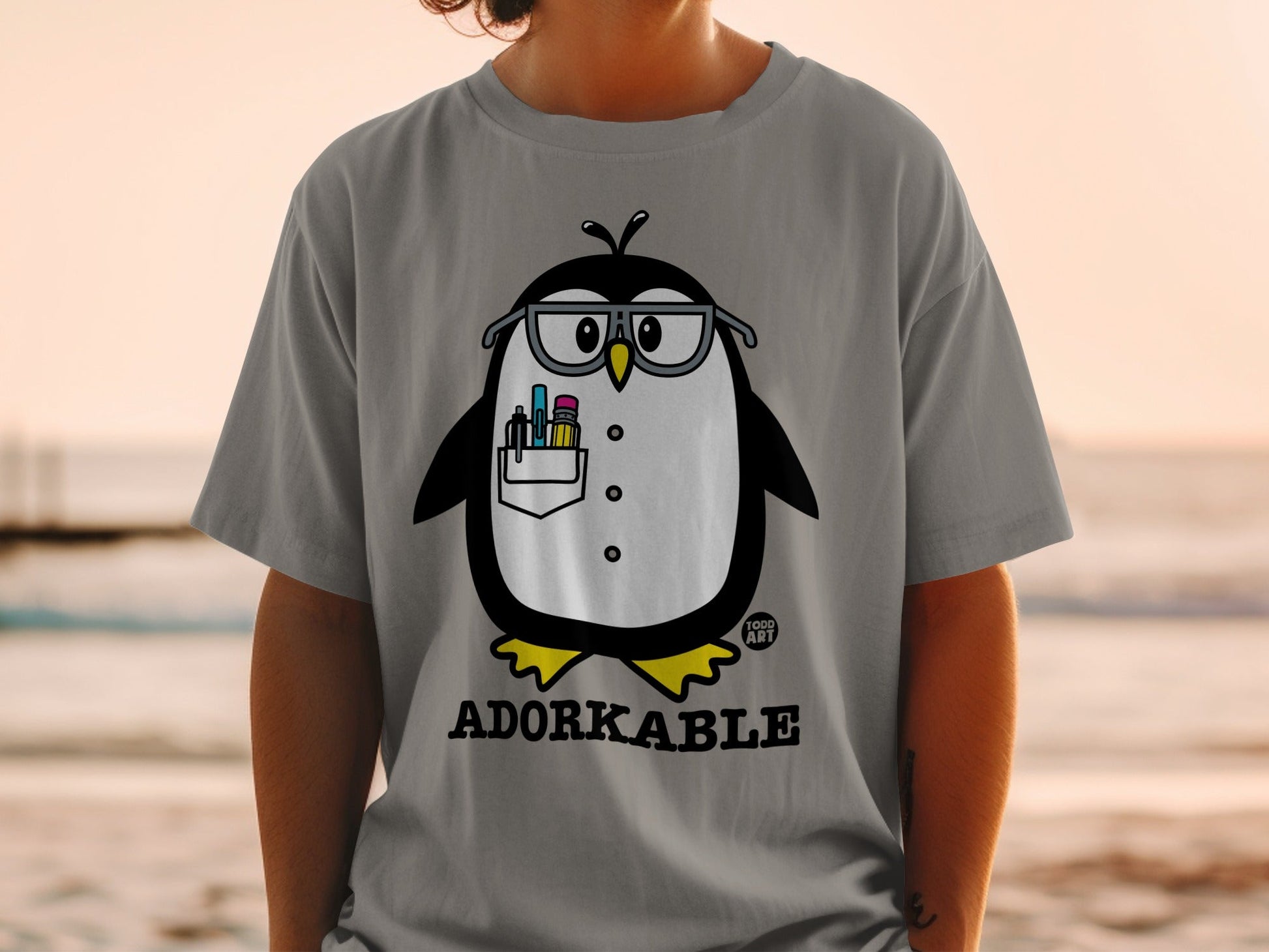 Grey t-shirt with cartoon penguin wearing glasses and holding pens.