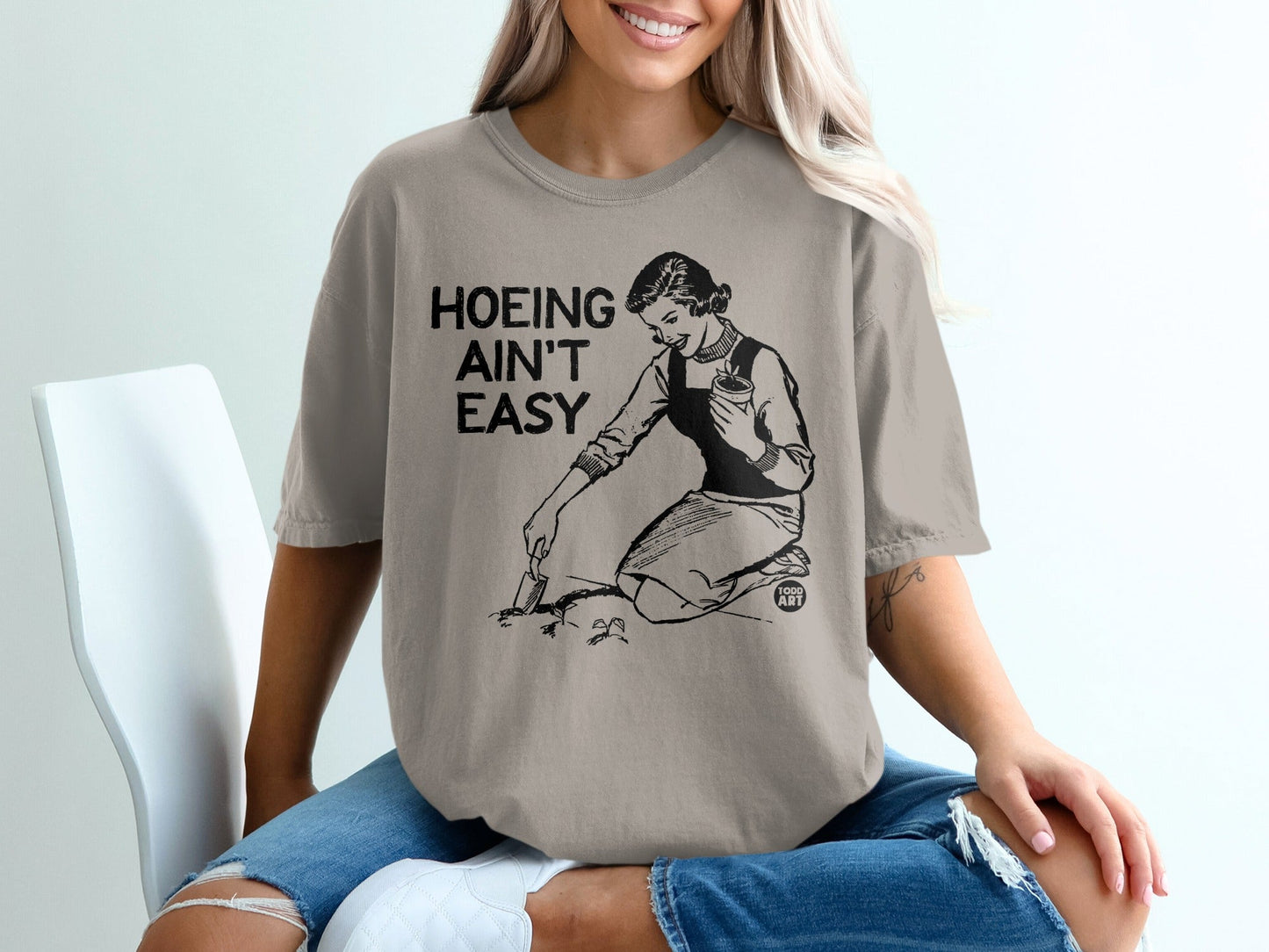 T-shirt with black text "Hoeing ain't easy" and a vintage illustration of a woman gardening.