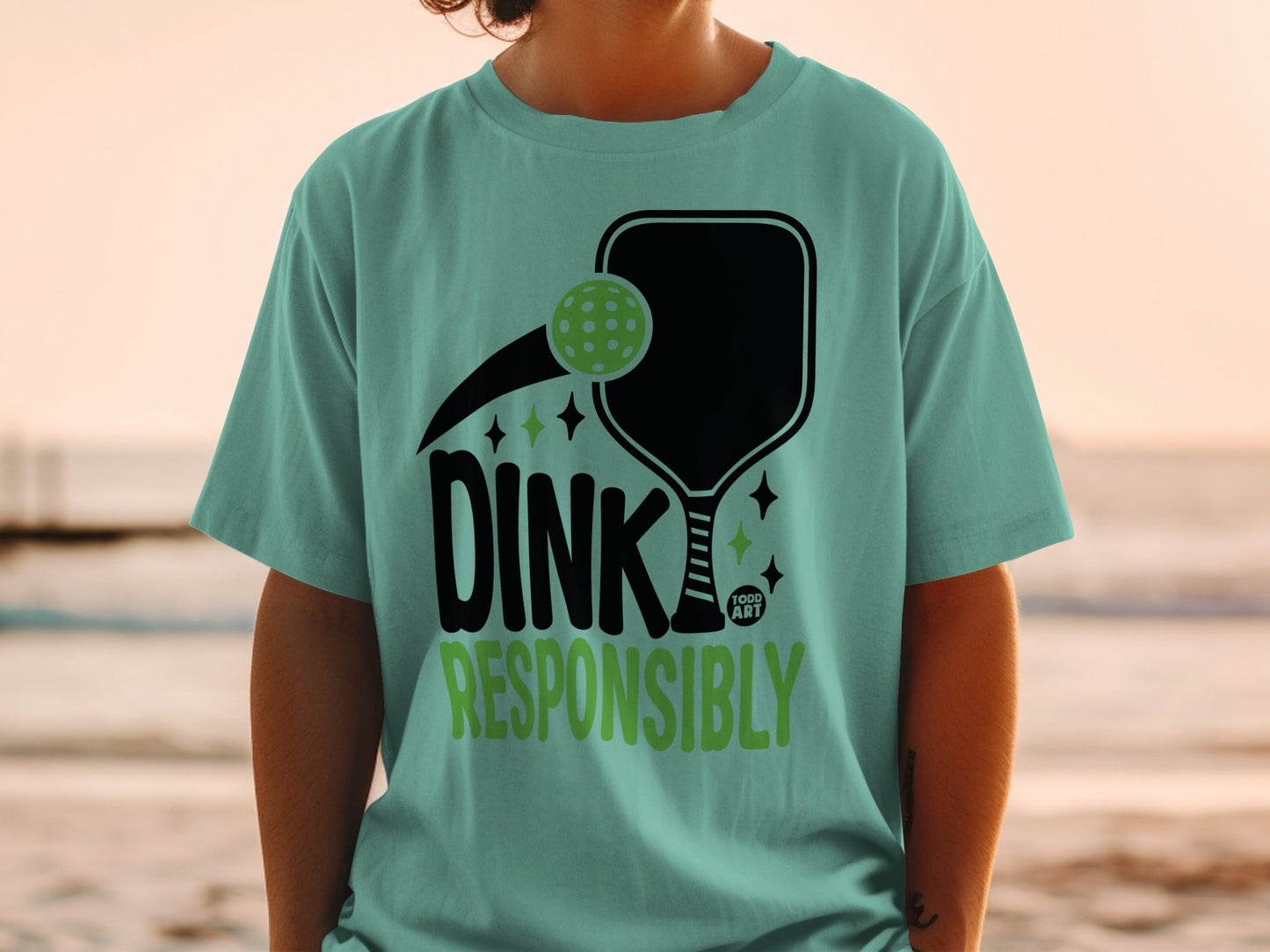 Light teal t-shirt with pickleball graphic and "Dink Responsibly" text.