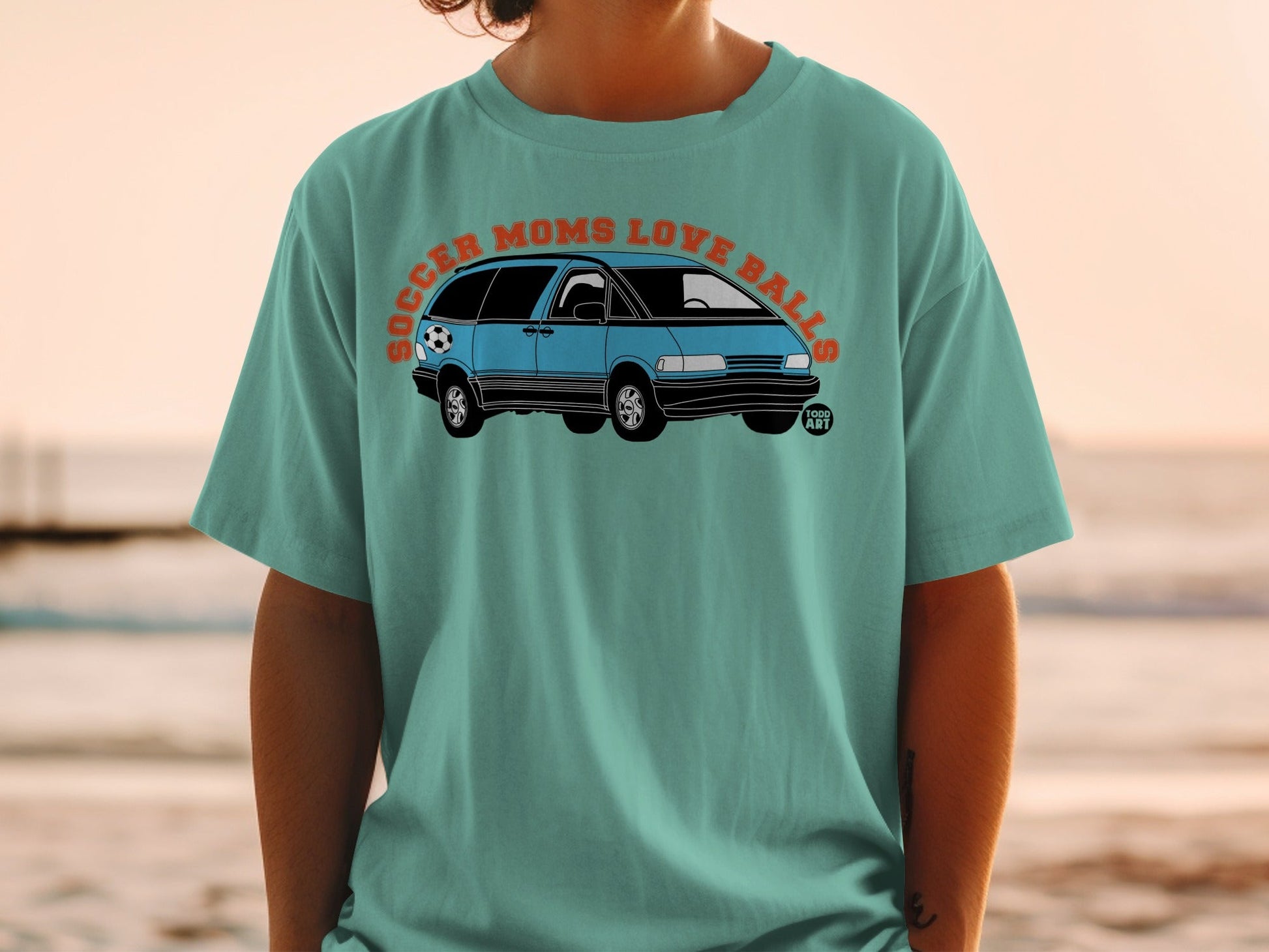 Teal t-shirt with blue minivan and soccer ball graphic, text "SOCCER MOMS LOVE BALLS".