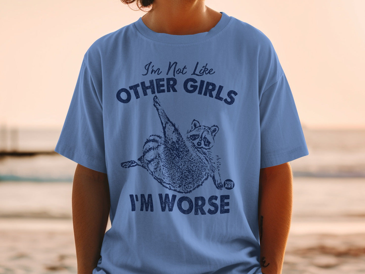 Blue t-shirt with a raccoon graphic and text "I'm Not Like Other Girls I'm Worse".