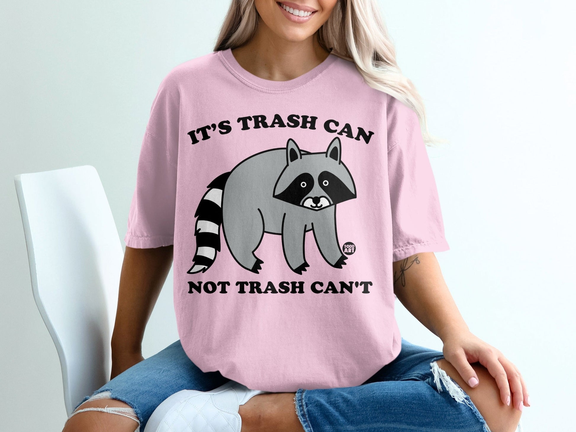 Pink t-shirt with raccoon graphic and "It's Trash Can, Not Trash Can't" text.
