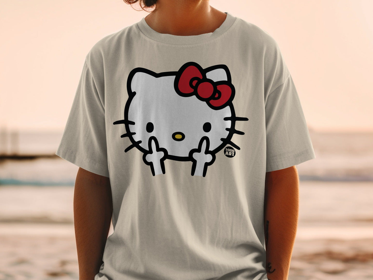 Hello Kitty graphic on a tan t-shirt, wearing a red bow, giving middle fingers.